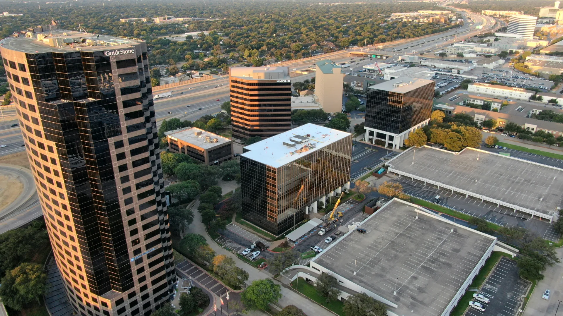 Aerial view of a Dallas commercial roofing project, with roofing materials on the rooftop and a crane beside the building