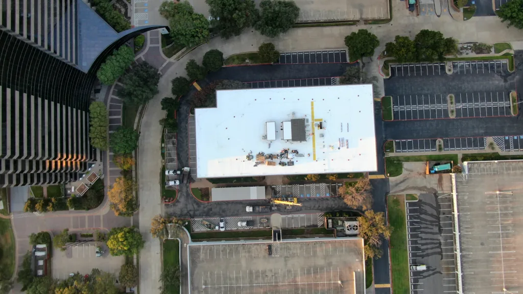 Overhead view of a Dallas commercial roof with rooftop equipment, staged materials, and a crane below